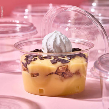 Coppetta in primo piano per monoporzioni, piena di dolce e aperta, tra tante coppette monoporzione chiuse e vuote, su sfondo rosa.